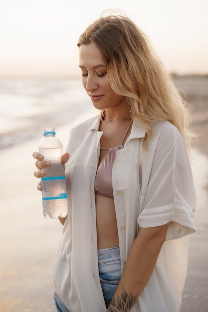 Young woman drinking water from the bottle on the beach