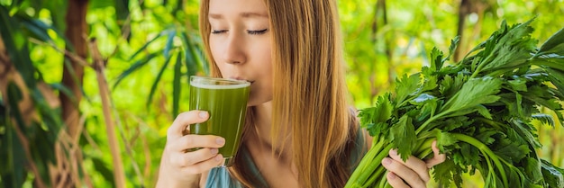 Young woman drinks celery juice healthy drink bunch of celery on a wooden background banner long