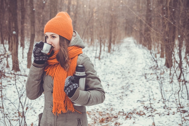 Young woman drinks tea in winter forest