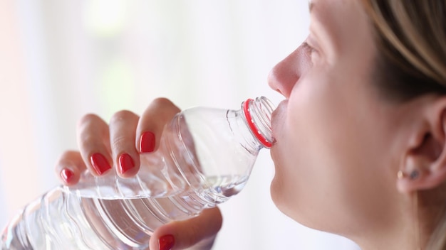 Young woman drinks water from bottle closeup