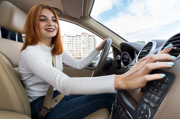 Young woman driving a car and adjusting the heater