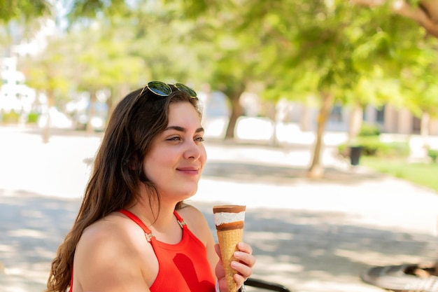 Young woman eating ice cream cone by the park on a sunny day of summer on holidays