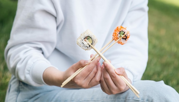 A young woman eating sushi in the park picnic in nature