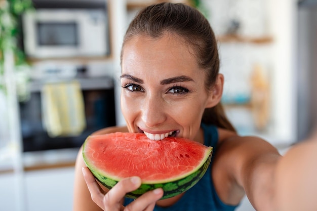 Young woman eats a slice of watermelon in the kitchen Portrait of young woman enjoying a watermelon