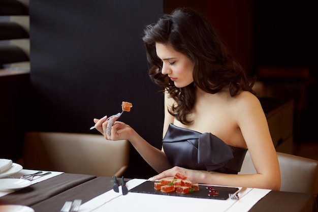 Young woman in elegant dress with bare shoulders serves a dessert in the restaurant with makeup and hairstyle