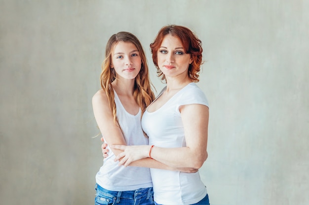 Young woman embracing teenage girl near gray wall