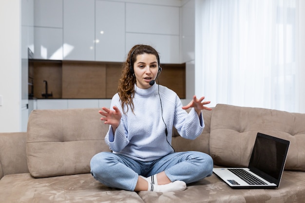 A young woman employee of a call center, provides online consultation staying at home, sitting on couch