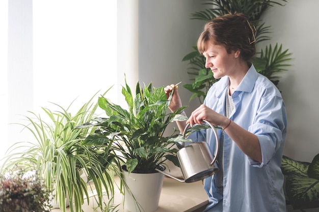 Photo a young woman enjoys caring for flowers watering indoor plants and admiring them