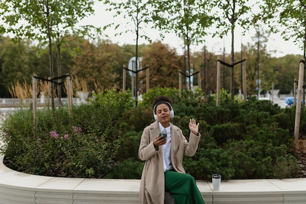 Young woman entrepreneur listens to music in headphones dance while sitting against the backdrop of