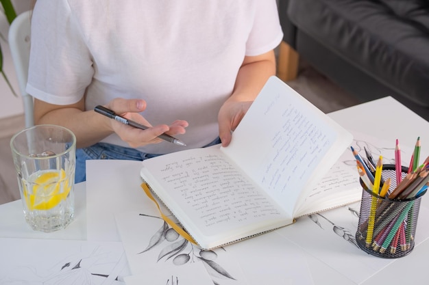 A young woman of European appearance does homework at school university The girl diligently studies at home at a white table Photography in light shades in a home interior