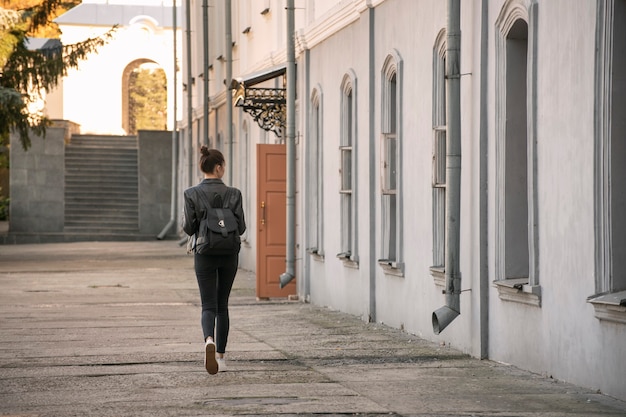 Young woman examines architecture. Student girl walks around the city. Tourist travel in the old yards. Back view.