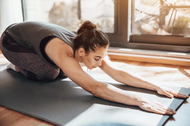 Young woman exercising at home in the morning. She is doing stretching workout on exercise mat.