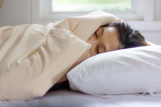 Young woman face sleeping while lying in white bed in Sunbeam dawn.