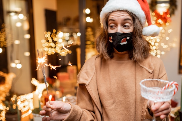 Young woman in facial mask celebrating alone New Year holidays at home. Concept of quarantine and self-isolation during the epidemic on holidays