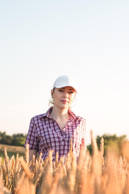 Young woman farmer works on a wheat field in the sun. Business woman plans her income in the field. Female agronomist with a tablet study the wheat crop in the agricultural field. Grain harvest.