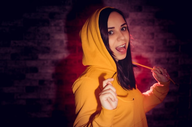 A young woman in a fashionable yellow hoodie Portrait of a beautiful brunette in a yellow hoodie against a brick wall