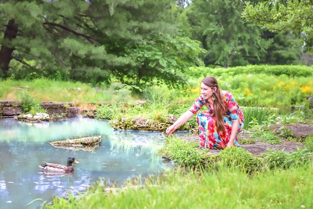 Photo young woman feeding duck in pond during spring