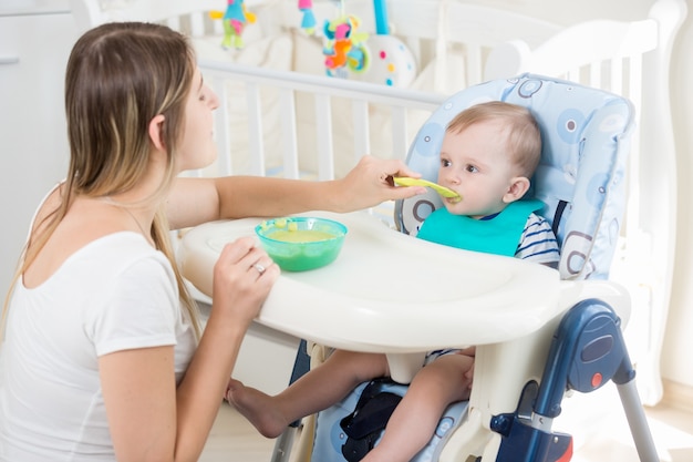 Young woman feeding her baby from spoon with apple sauce