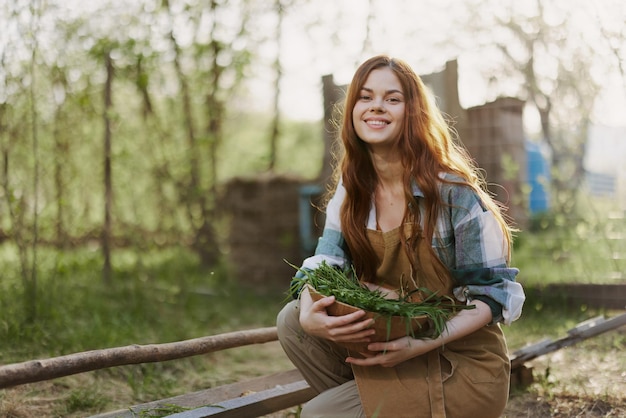 A young woman feeds her chickens on the farm with grass wearing a simple plaid shirt pants and apron and smiling for the camera caring for the animals High quality photo