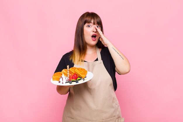 Young woman feeling happy, excited and positive, giving a big shout out with hands next to mouth, calling out