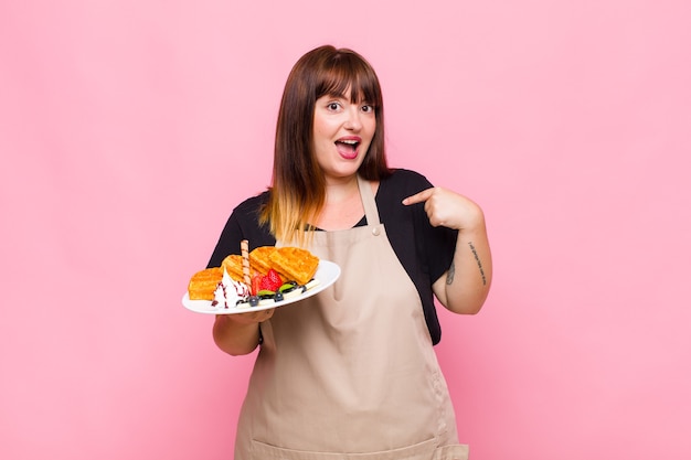 Young woman feeling happy, surprised and proud, pointing to self with an excited, amazed look