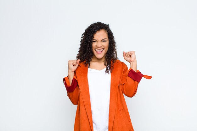 Young  woman feeling happy, surprised and proud, shouting and celebrating success with a big smile against white wall