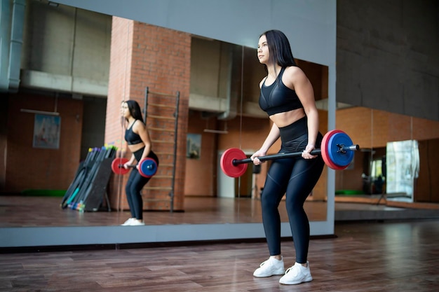 Young woman in the fitness room with a barbell female girl trains with power loads sports