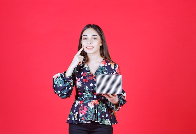 Young woman in floral shirt holding a silver gift box