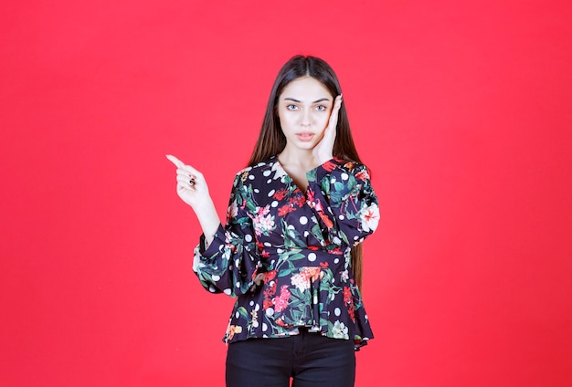 Young woman in floral shirt standing on red wall and showing left side