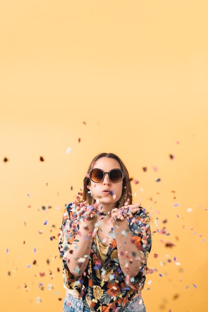 Young woman in a flowered shirt and big round sunglasses blowing confetti