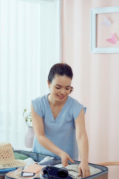 Young woman folding clothes and placing inside maroon luggage isolated indoors background