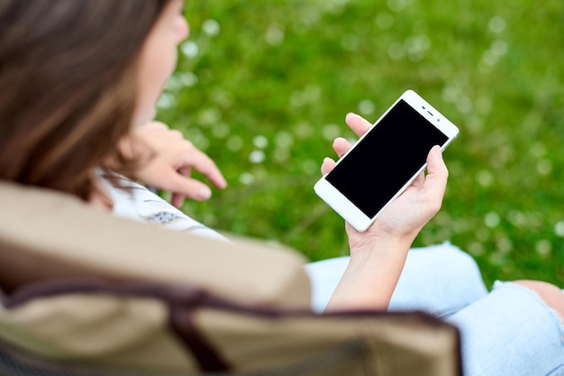 Young woman freelancer sitting on chair and using smart phone Remote work and Relaxing in nature Black screen background place for text