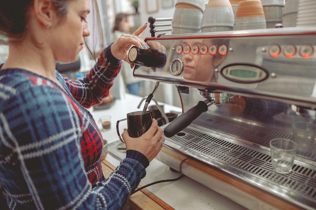 Young woman frothing milk for latte in coffee machine