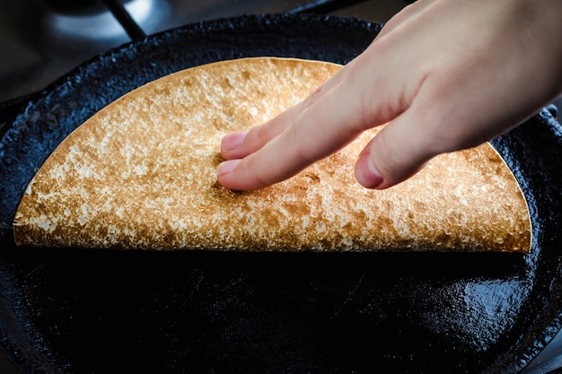 Young woman frying quesadilla in a frying pan