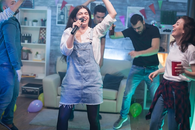 Young woman full of joy singing on microphone at the party with her friends.