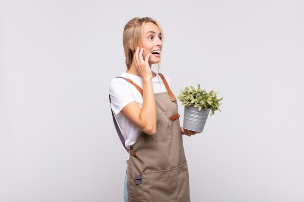 Photo young woman gardener feeling happy, excited and surprised, looking to the side with both hands on face