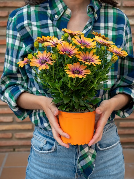 Young woman gardening at home holding pot with flowers