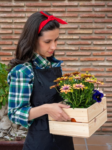 Young Woman Gardening At Home with flower pot into wooden box