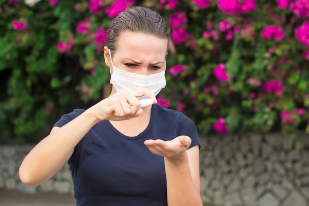 Young woman girl disinfects hands, girl in protective sterile medical mask on face