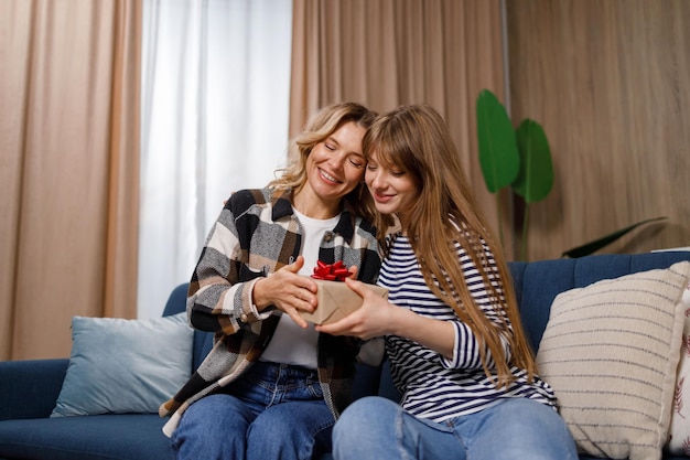 Young woman giving her mother gift box at home