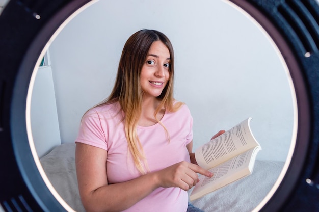 Young woman giving online classes looking at the camera and showing information from a book