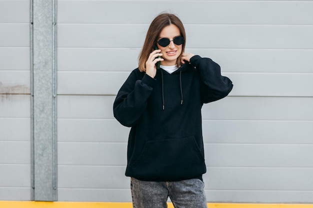 Young woman in glasses and black hoodie with mobile phone