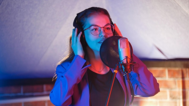 A young woman in glasses singing in neon lighting in the studio