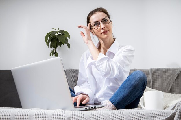 Young woman in glasses with laptop with coffee sitting on sofa