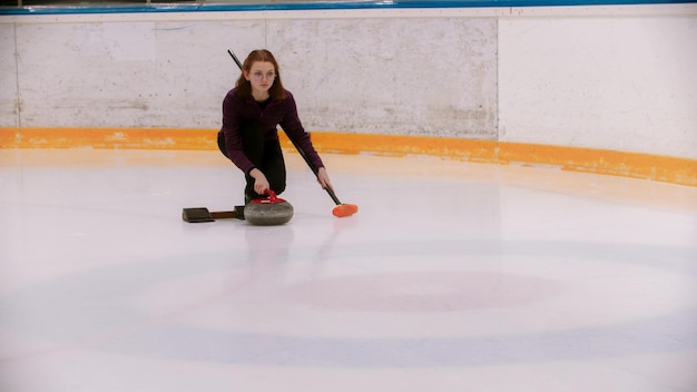 A young woman in glasses with short hair playing curling