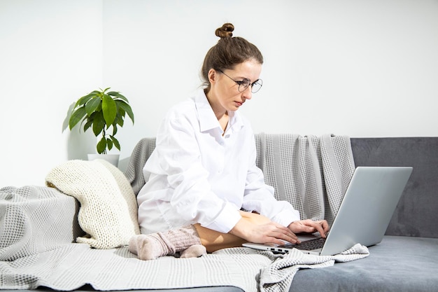 Young woman in glasses working with laptop sitting on sofa