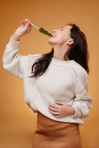 Young woman gnaws sweet caramel in the form of a christmas tree on a yellow background