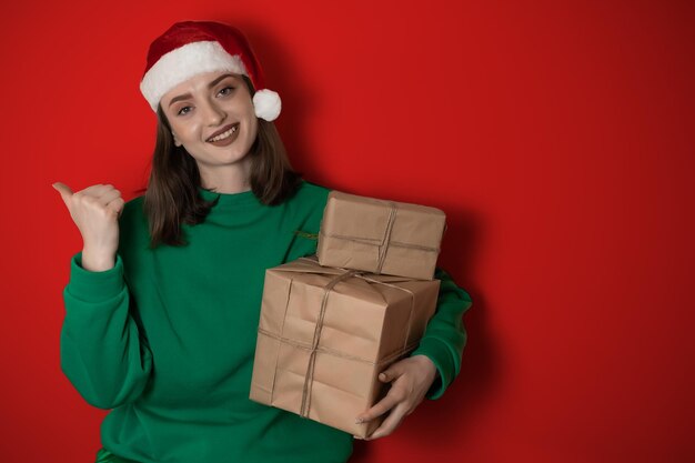 Young woman in a green sweater and in a New Year's hat holds a gift box on a simple green background Holiday concept Happy New Year 2023 chrome key merry christmas