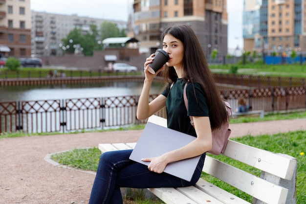 Young woman in a green T-shirt and a backpack sitting on a wooden bench