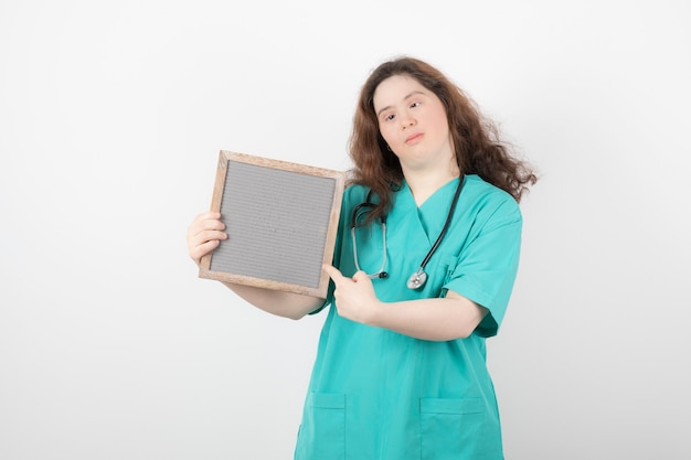 young woman in green uniform pointing at a frame.